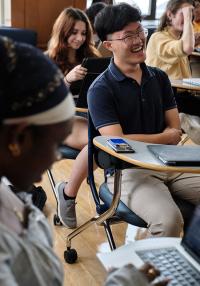 A young man with glasses in a classroom laughs